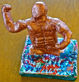 Foto på skulptur av en gyllene figur som tycks växa fram ur en mångfärgad lera. Foto på skulptur av en gyllene figur som tycks växa fram ur en mångfärgad lera.
