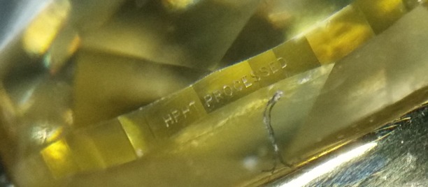 Bilden visar laserinskription i rondisten hos en gul diamant som fått sin fancy gula färg genom hpht behandling. Foto Jan Asplund. Bilden visar laserinskription i rondisten hos en gul diamant som fått sin fancy gula färg genom hpht behandling. Foto Jan Asplund.