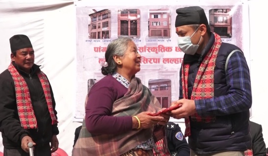 Vår projektledare Shekhar och en av kvinnorna i Nepal som fått flytta in i ett av de nybyggda, jordbävningssäkra husen i traditionell stil efter jordbävningen. I bakgrunden syns en plansch med några av husen. Vi måste förstås inte flyga för att hjälpa människor i andra länder.