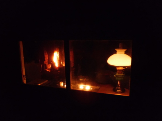 Höstkväll i Arvidssonstugan, med fotogenlampa, stearinljus och eld i den öppna spisen.