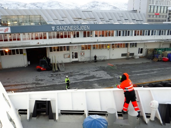 En besättningsmedlem ur MS Vesterålens besättning kastar en liten tamp (som är fäst i en större tamp) till hamnpersonalen på land som ska hjälpa till att förtöja MS Vesterålen i Sandnessjøen.