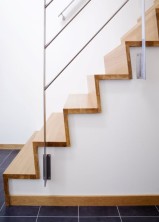 Tät "Z-trappa" med steg och sättsteg i mattlackad ek. Underliggande vangstycken i vitmålad furu. Räcke 1 i rostfritt stål.