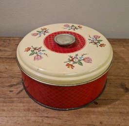 Rund burk med "knopp" på locket. Rödrutig runt sidan och rosmotiv på locket. Diam. ca 20 cm, höjd 9 cm. 80 SEK