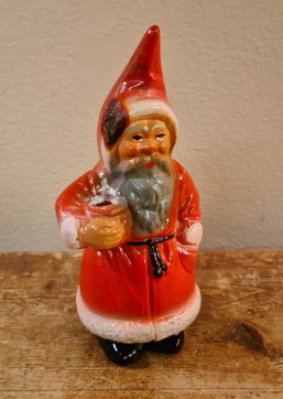 Tomte med röd rock och grått skägg. Höjd ca 15 cm. Svedd fläck på luvan, annars gott skick. 100 SEK