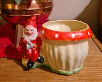 Sittande tomte vid flugsvamp. Höjd 11,5 cm, bredd ca 16 cm. Lagad vid luvan, annars gott skick. 90 SEK