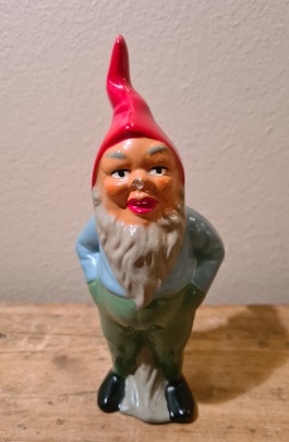 Stående tomte med händerna i fickorna, blå tröja och gröna byxor. Lite skadad näsa, annars gott skick. Höjd 15,5 cm. 65 SEK