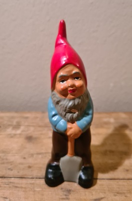 Liten stående tomte med spade. Höjd ca 12 cm. Limmat huvud samt en nagg på hälen (ifärgad). 50 SEK