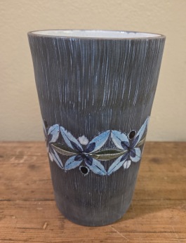 Rak gråblå vas med blommönster på mitten. Höjd ca 15 cm, diam. upptill 10 cm. Mininagg på kanten (ifärgad), annars gott skick. 75 SEK