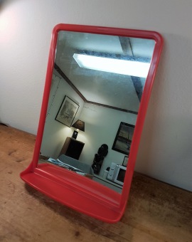 Spegel i röd plast med hylla. Höjd 37,5 cm och bredd 26 cm.  125 SEK