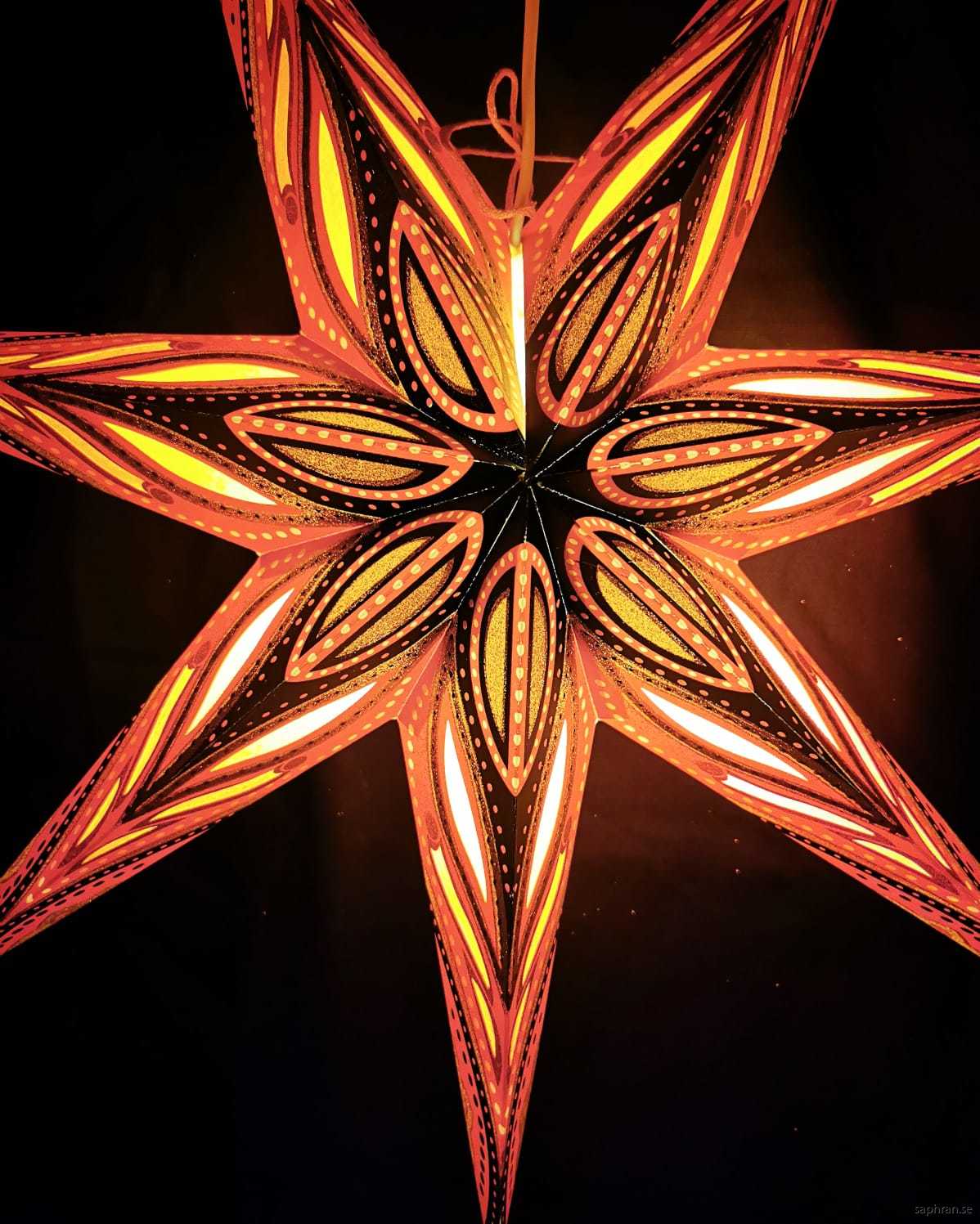 Guldglittrig adventsstjärna med mönster i svart och oranget
