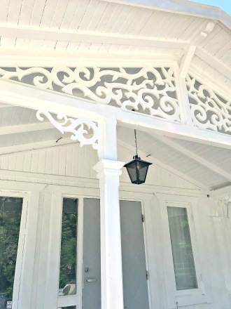En vit farstukvist och veranda med mycket snickarglädje och husdekoration, träkonsoler och fyllnadsdekor med ornament och blad i nock.