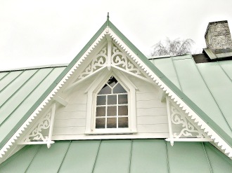 En vitmålad takkupa med grönt koppartak med mycket snickarglädje och husdekoration i nock.