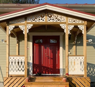 En beige farstukvist och veranda med mycket snickarglädje och husdekoration, träkonsoler, trappräcke och fyllnadsdekor i nock.