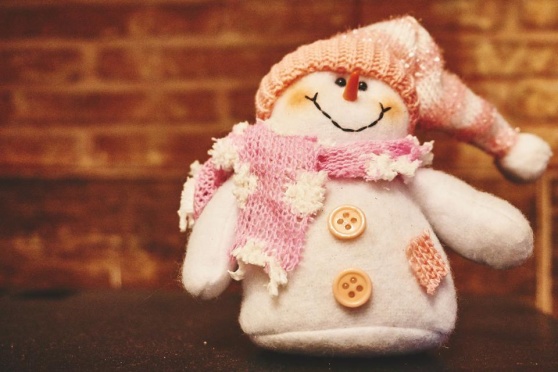 Syntolkning: En glad snögubbedocka med morotsnäsa och rosavit halsduk.