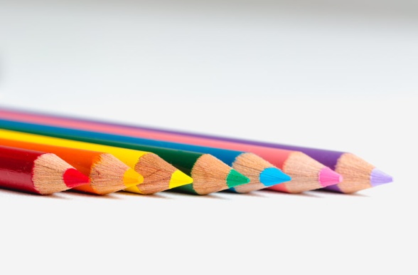 Närbild på sju nyvässade blyertspennor i regnbågens färger som ligger på ett vitt bord.