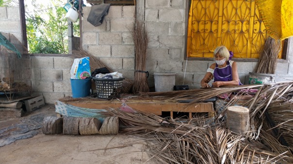 Den gamla damen gör tunna strimlor till sopkvastar av palmblad.