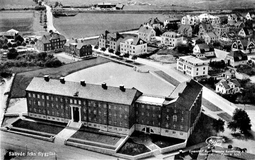 I bildens överkant ser man SAJ-banans korsning med Varnhemsvägen och de båda stugorna, ekonomibyggnaderna på det lilla industriområdet. Mäktigt bygge 1930 av Nya Läroverket. (Skövde Stadsmuseum)