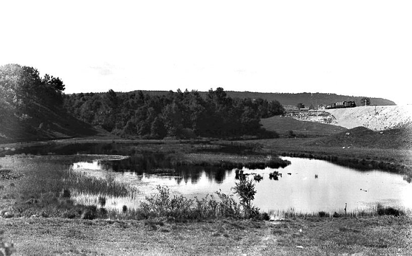 Harkessjön 1905 enligt bildtext i arkivet. Med Axevalla-tåget på väg mot Skövde som just lämnat banvaktstugan vid Varnhemsvägen (Skövde Stadsmuseum)