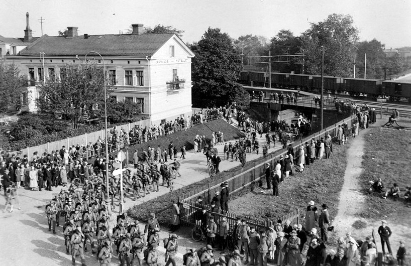 1930-tal; militären är viktig för Skövdeborna. Här stor uppslutning vid marsch under SAJ-bron. Vackert Järnvägshotell och ordnat kring gator och grönområde - SAJ's frilastområde. (Skövde Stadsmuseum)